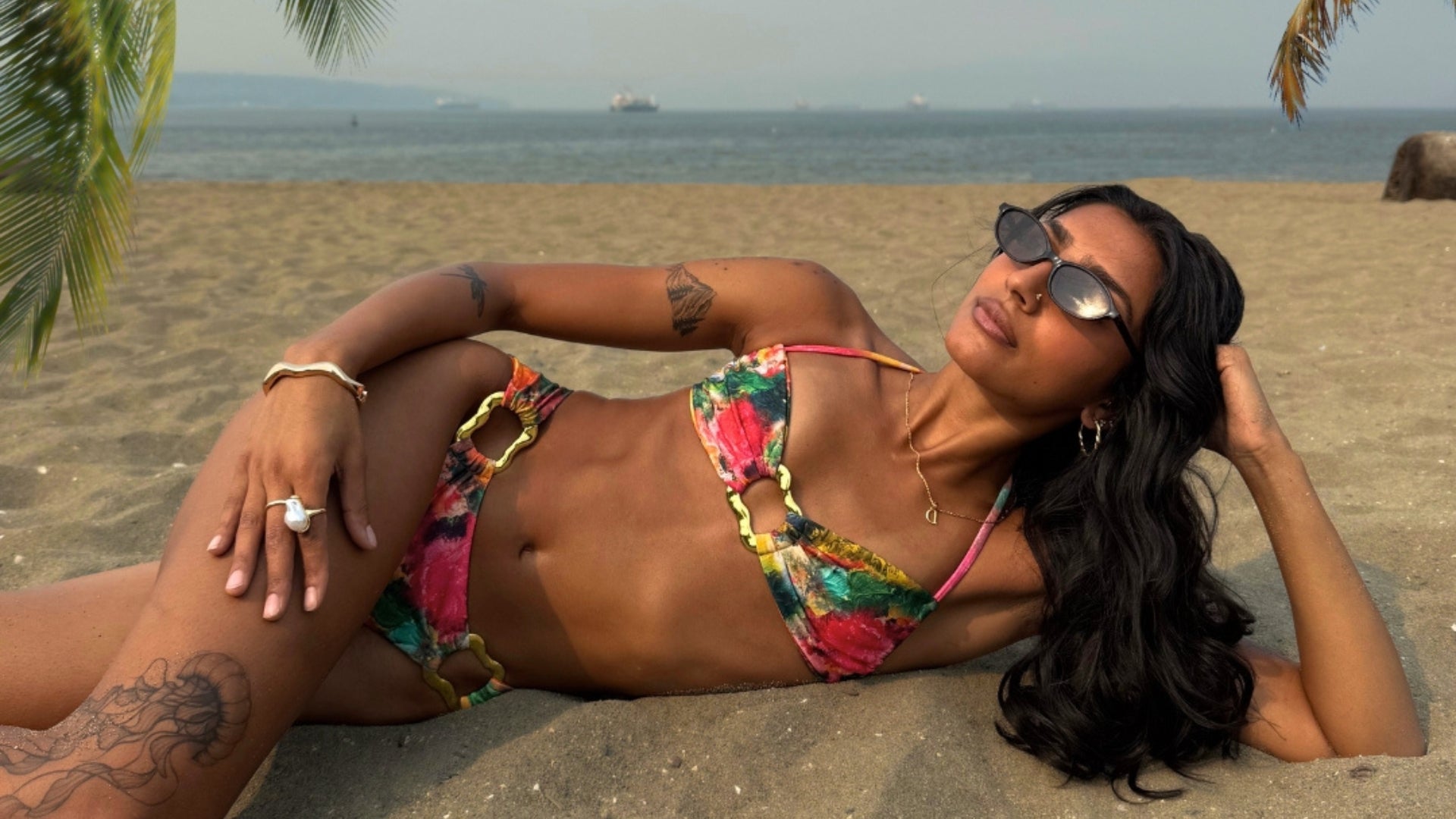 Woman in a colorful bikini lying on a beach with palm trees and ocean in the background