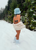 Person in a snowy landscape wearing a colorful bikini with a blue hat and boots.