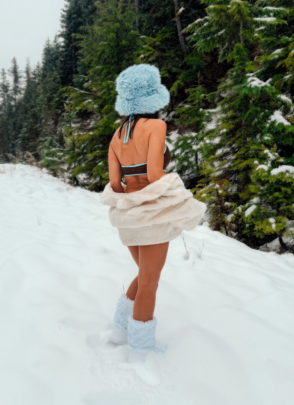 Person in a snowy landscape wearing a colorful bikini with a blue hat and boots.